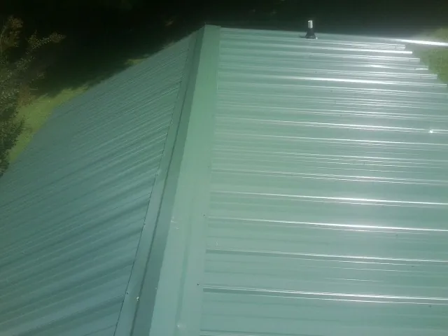 New green metal panels meeting at the ridge of a roof — Flat Roof Repair work by our crew in Montezuma
