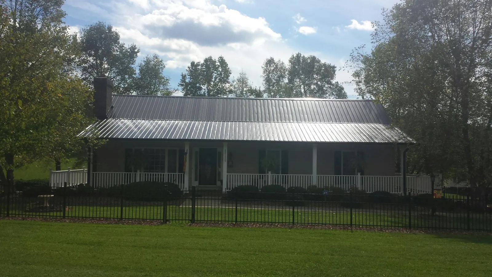 Gray metal roof on a brick ranch with a full width front porch — Gutter Guard Installation work by our crew in Montezuma