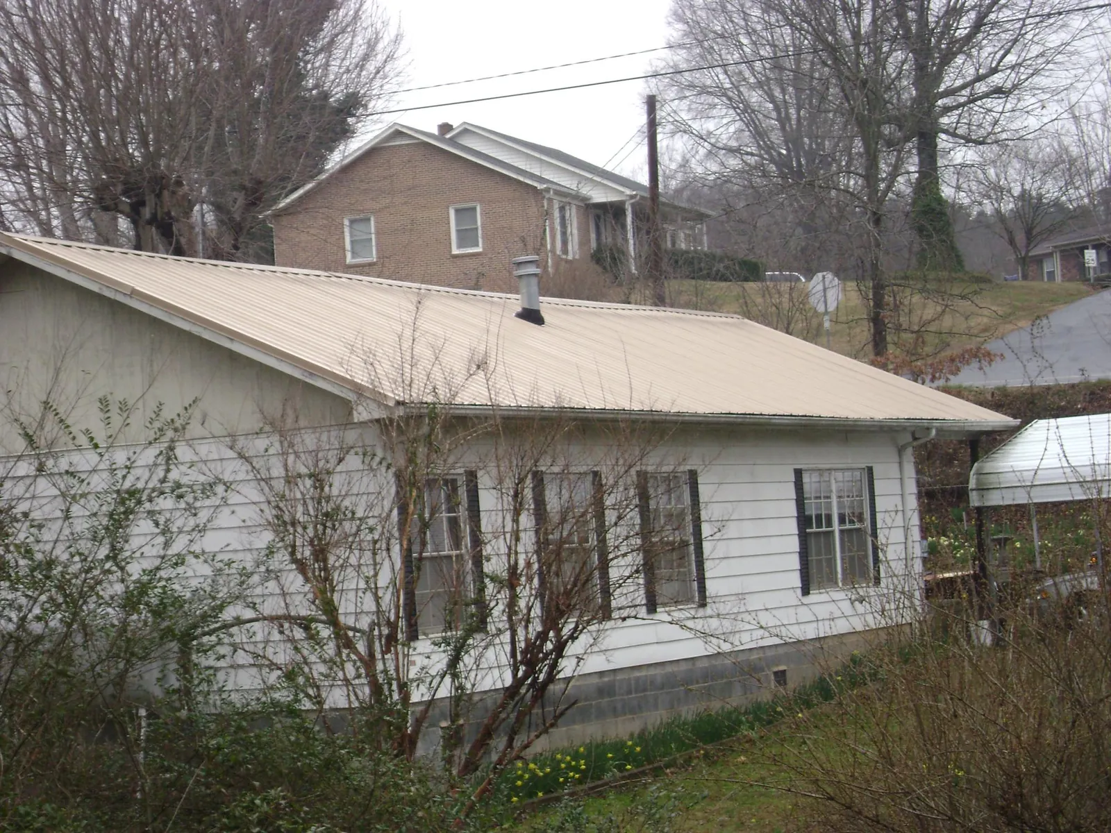 Tan metal roof on a white sided house set into a hillside — Commercial Roofing by Roofing Brothers in Montezuma